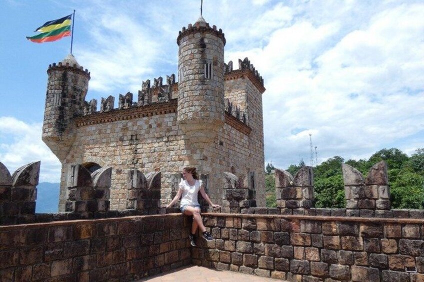 A stone castle with a flag, a person sitting on a wall, and a clear sky. 5