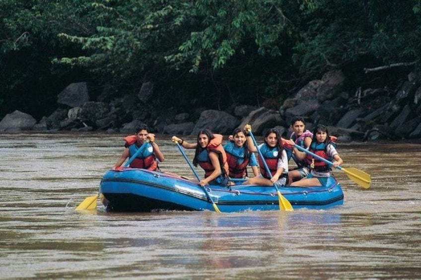 A group of people in a blue raft on a river surrounded by rocks and trees. 1