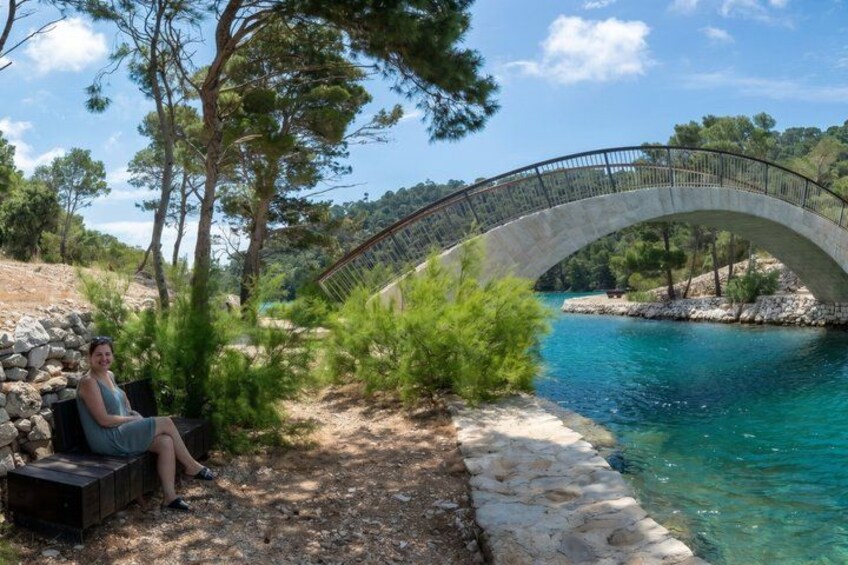 A stone bridge over a turquoise body of water, surrounded by trees and a rocky path. 1