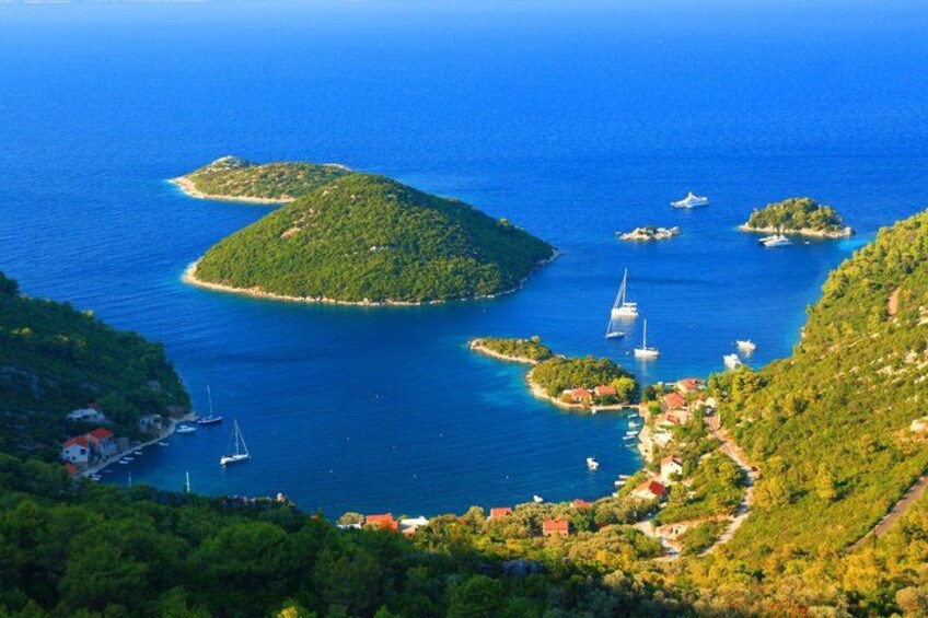 A coastal landscape with a prominent island, clear blue waters, and several sailboats. 3