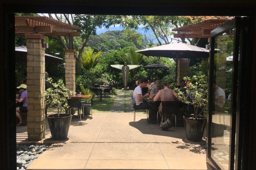 An outdoor patio with tables and chairs, surrounded by potted plants and a pergola structure. 2