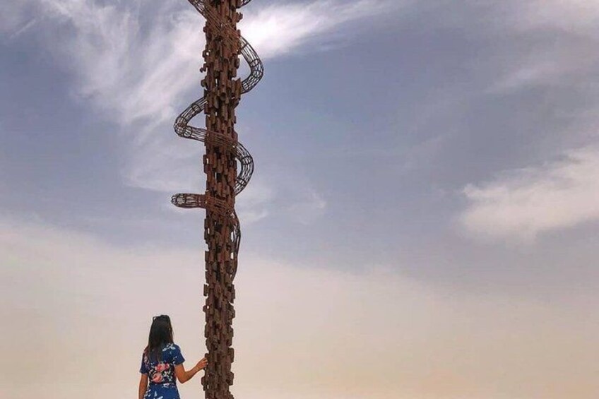 A person standing next to a tall, abstract sculpture against a sky with clouds. 3