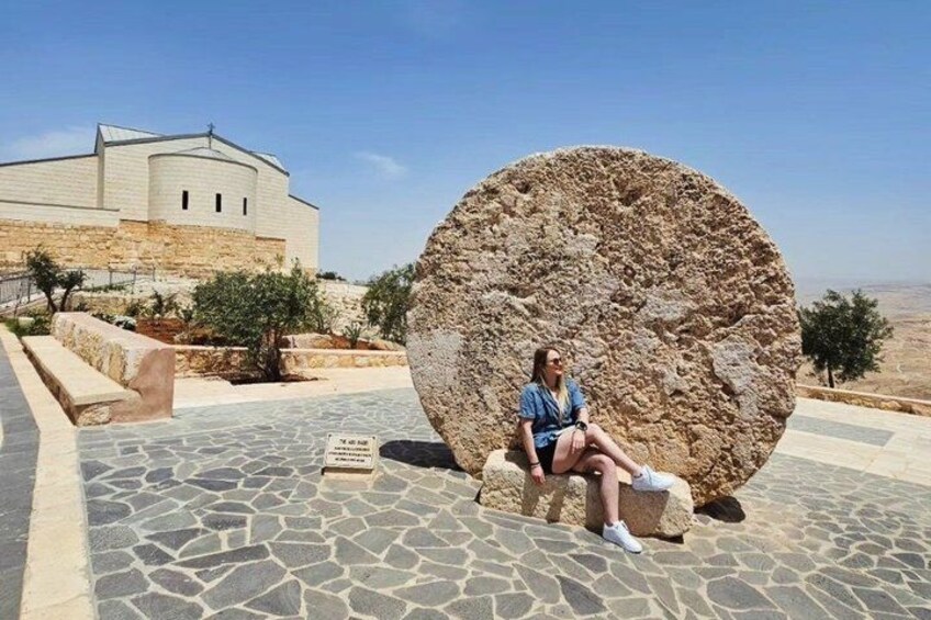 A person sitting on a stone bench with a large rock sculpture nearby, a building in the background, and a clear sky. 2