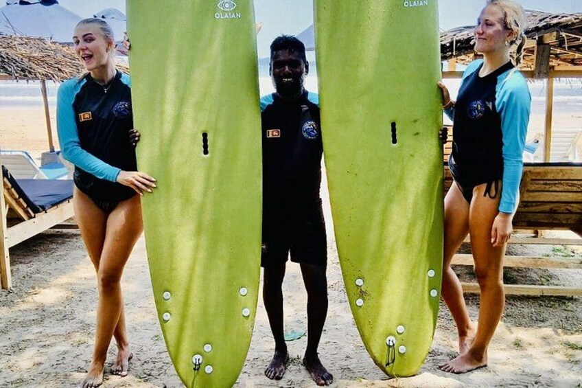 Three people holding surfboards on a sandy beach with a wooden structure in the background. 4