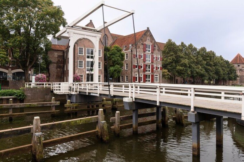 A wooden bridge over a canal, a historic building with red windows, and a tree-lined background. 3