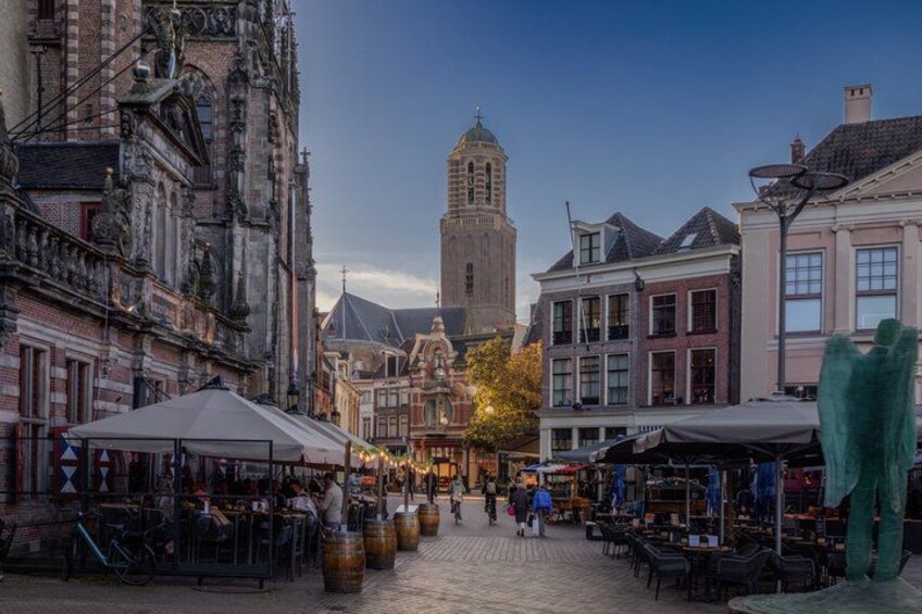 A cobblestone street lined with historic buildings, a prominent tower, and outdoor market stalls. 4