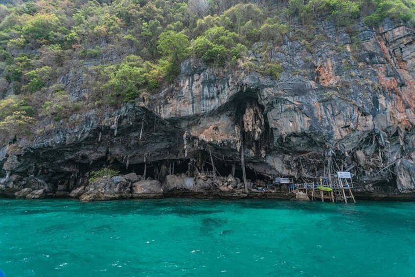A coastal cliff with a cave entrance, turquoise water, and a small dock. 5