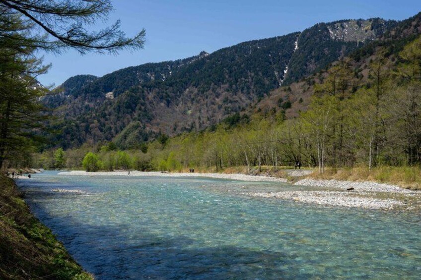 A clear river with a rocky riverbed, surrounded by trees and mountains. 2