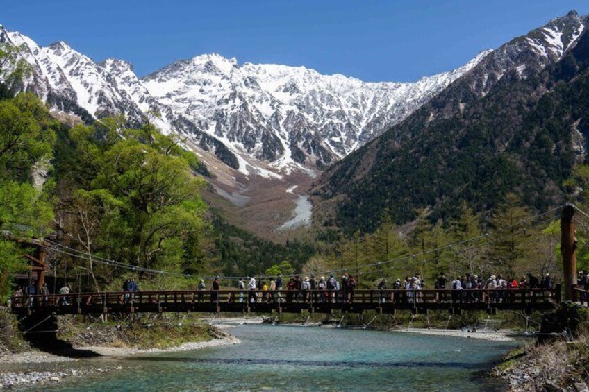A wooden bridge over a river with snow-capped mountains in the background. 1