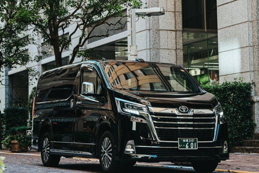 A black Toyota Hiace van parked in front of a modern building with large windows and a stone facade. 2
