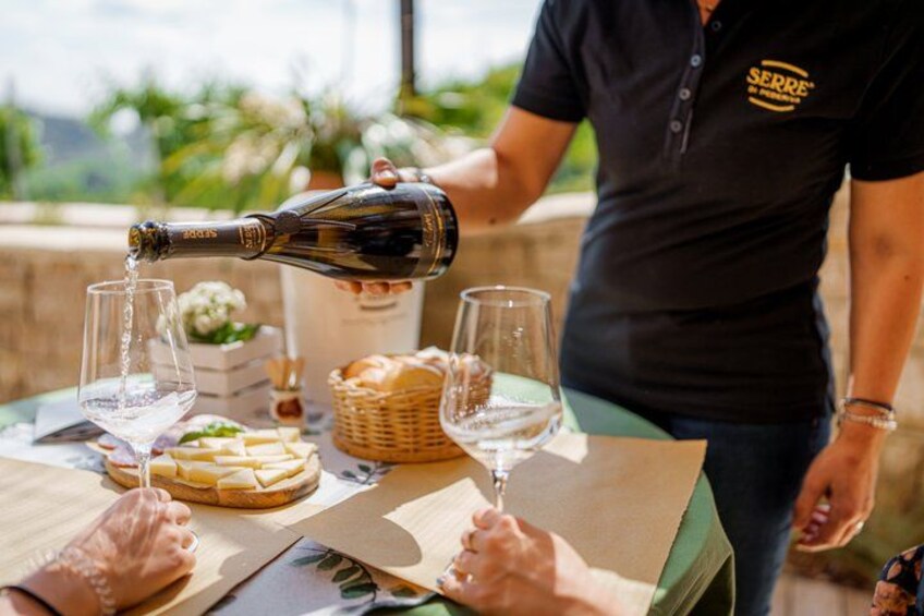 A person pouring wine into a glass, a bottle, and a basket of bread on a table. 3