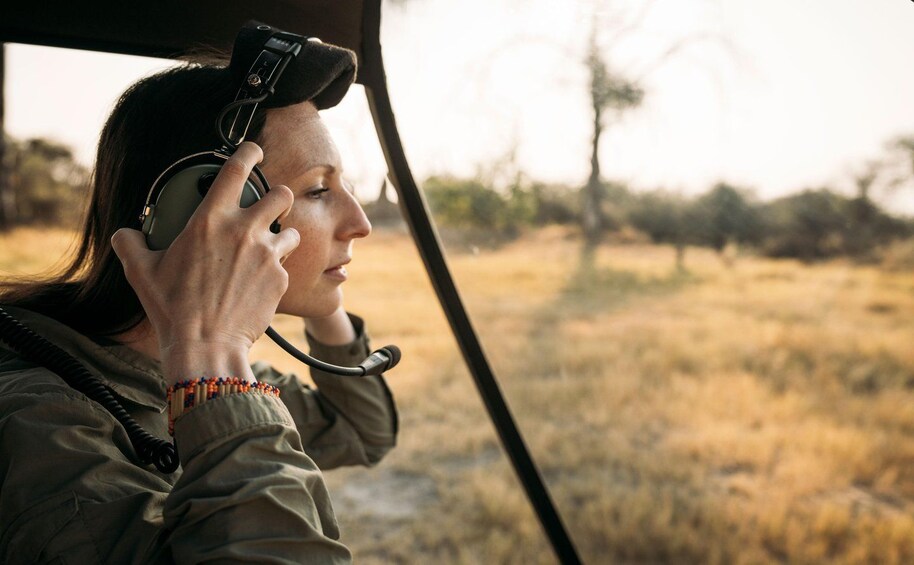 A person wearing a headset, holding a device, and looking out of a vehicle. 2