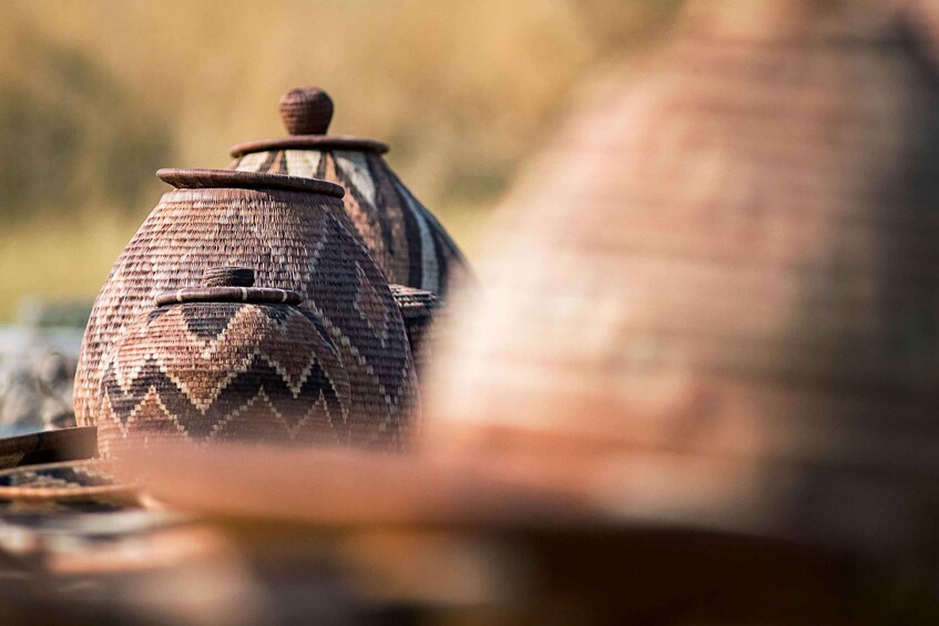 A close-up of a traditional woven pot with a lid, set against a blurred natural background. 3
