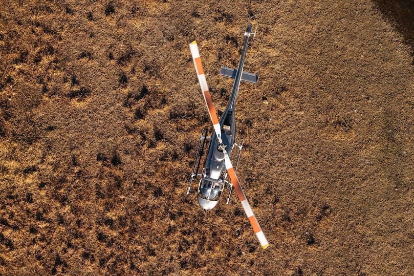 Ein Hubschrauber mit orangefarbenen und weißen Streifen fliegt über ein trockenes, saftiges Feld. 3