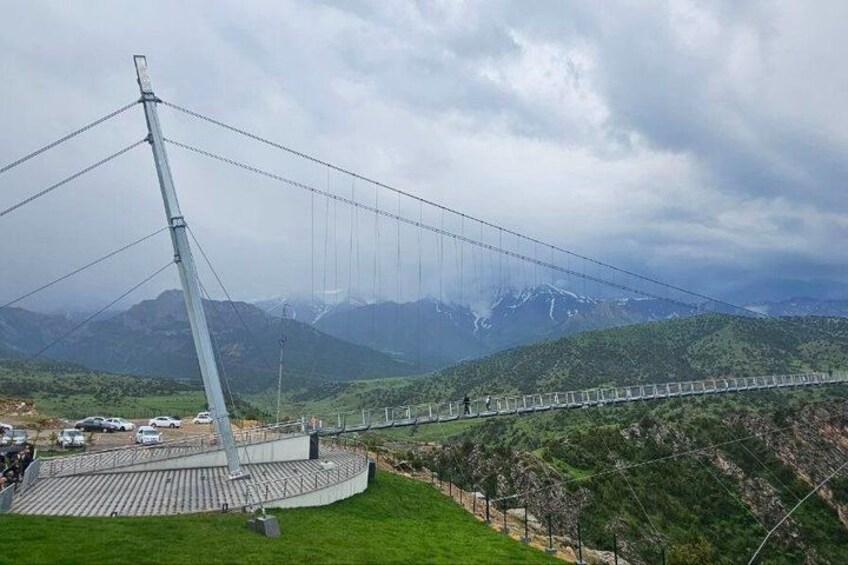A suspension bridge with cables, a paved walkway, and a mountainous landscape in the background. 4