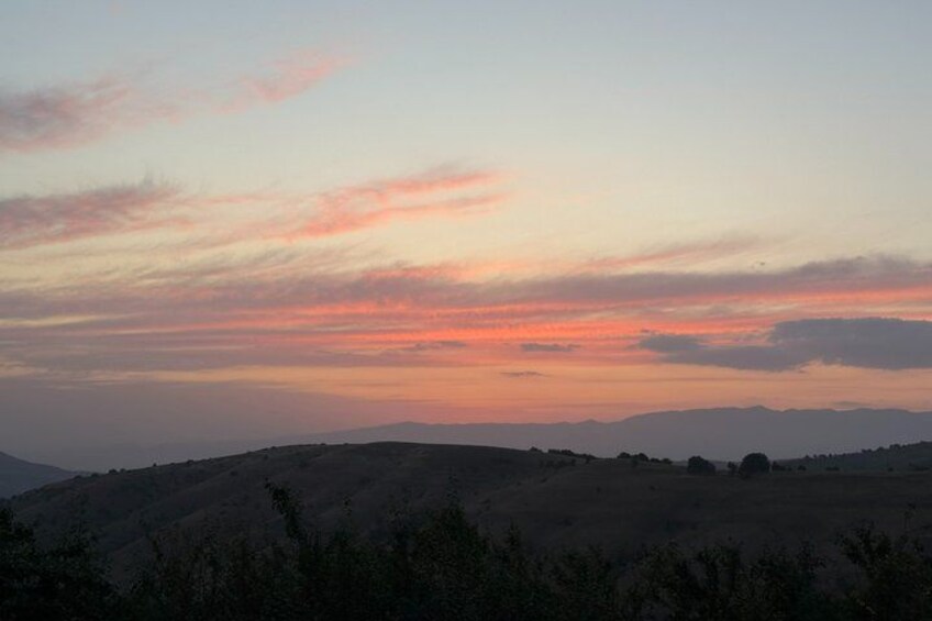 A sunset over a hilly landscape with sparse vegetation. 5