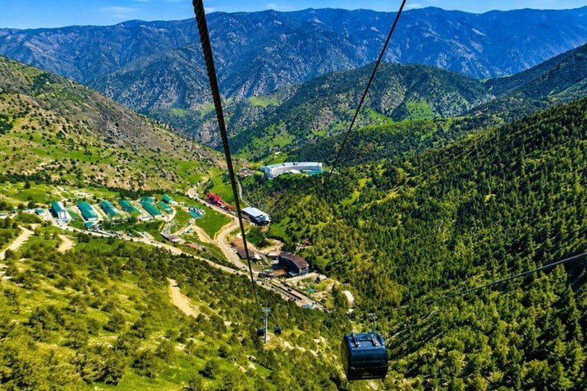 A cable car system in a mountainous area with green valleys and a distant building. 1