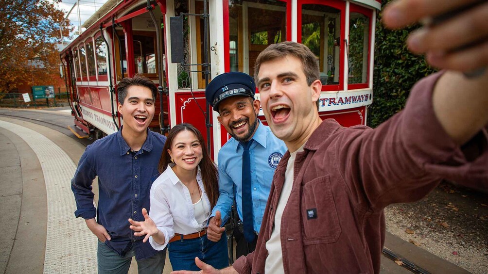 A group of people taking a selfie in front of a red tram. 5