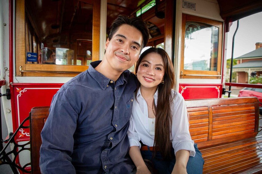 A man and a woman sitting on a bench inside a red and white train carriage. 4