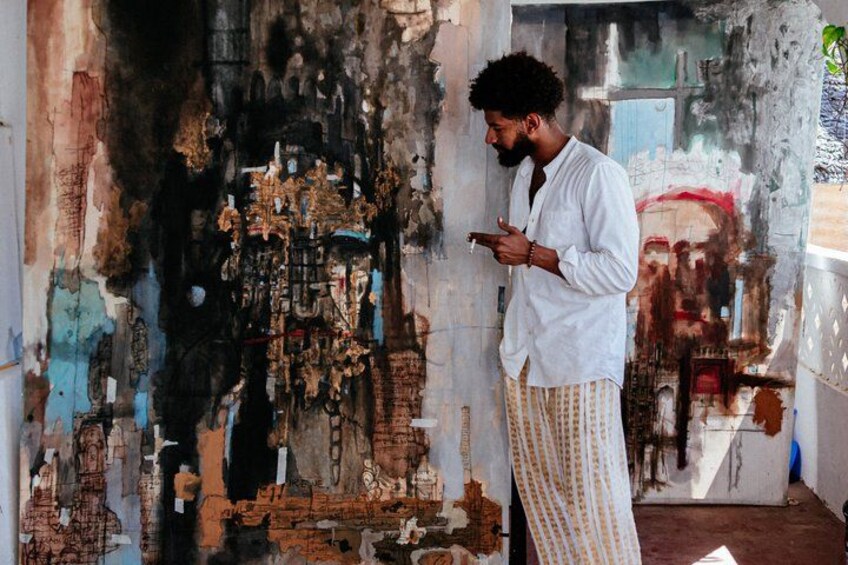 A person standing indoors, wearing a white shirt and patterned pants, looking at a mobile device. 1