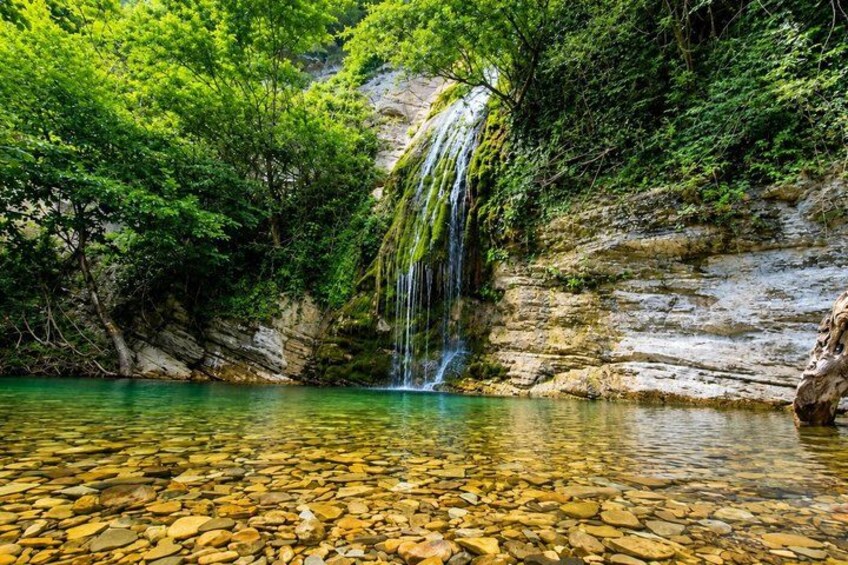 A clear water body with a waterfall, surrounded by green foliage and rocky terrain. 2