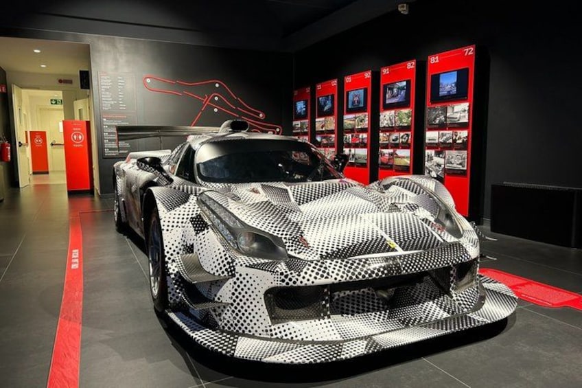 A sports car with a distinctive black and white pattern, displayed in a showroom with red accents and informational panels. 3