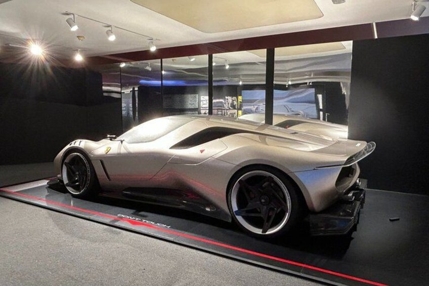 A silver sports car on display in a modern, dimly lit showroom with a red stripe on the floor. 4