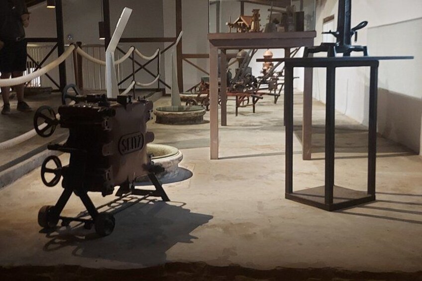 An indoor exhibition with vintage machinery, including a large mechanical device with wheels and a smaller table with a tool on it. 3