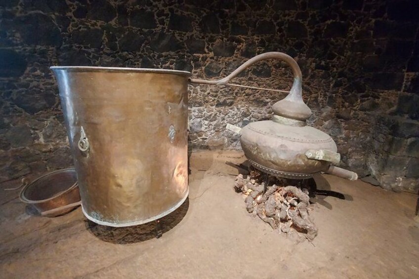 A large metal pot and a stove with a chimney, placed on a stone floor. 5