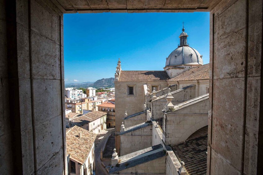 A view through a stone archway of a cityscape with a prominent dome and tiled rooftops. 4