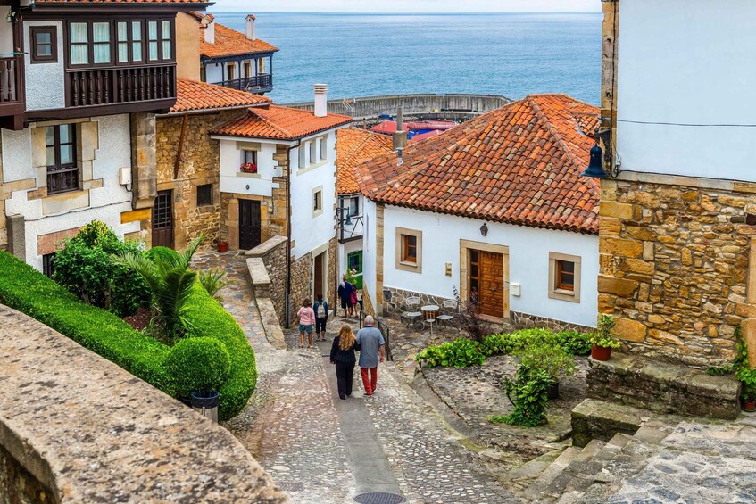 Una estrecha calle adoquinada en un pueblo costero con edificios de tejados de terracota y vistas al mar. 2