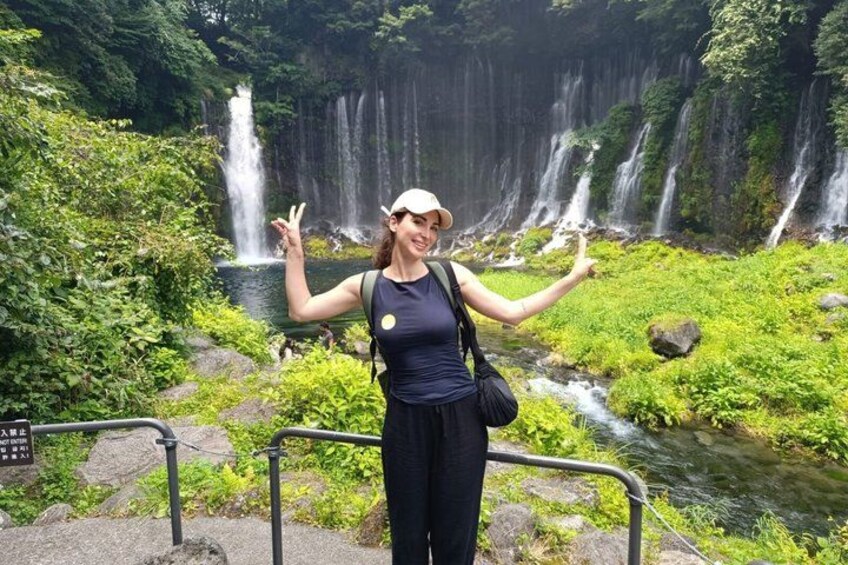 A person standing in front of a waterfall with greenery and a stream. 2
