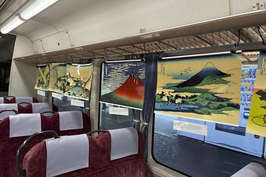 A train interior with seats covered in red fabric and artwork on the windows. 5