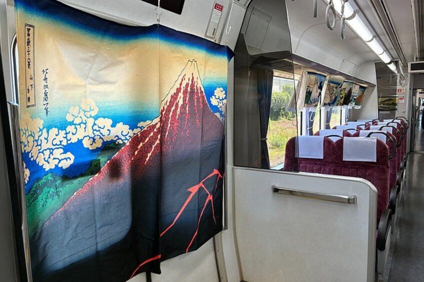 A train interior with seats, a view of Mount Fuji, and Japanese artwork. 2