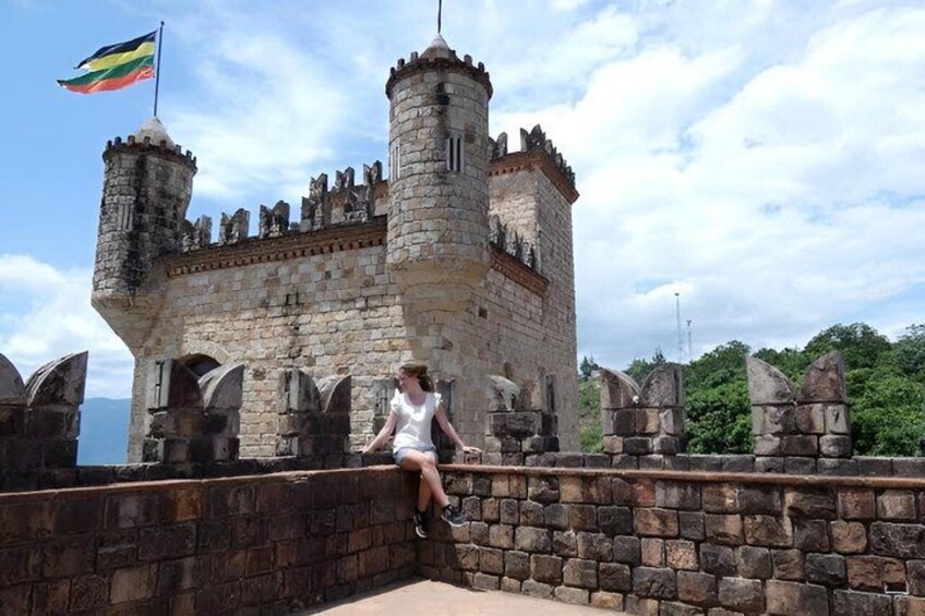 A historic stone castle with a flag, a person sitting on a wall, and a clear sky. 3
