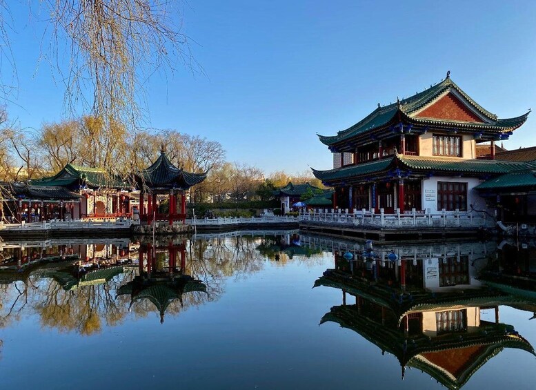 Traditionele Chinese architectuur, weerspiegeld in het water, onder een heldere lucht en kale bomen. 4
