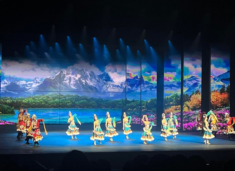 A stage performance with dancers in colorful costumes against a backdrop of a mountainous landscape. 5