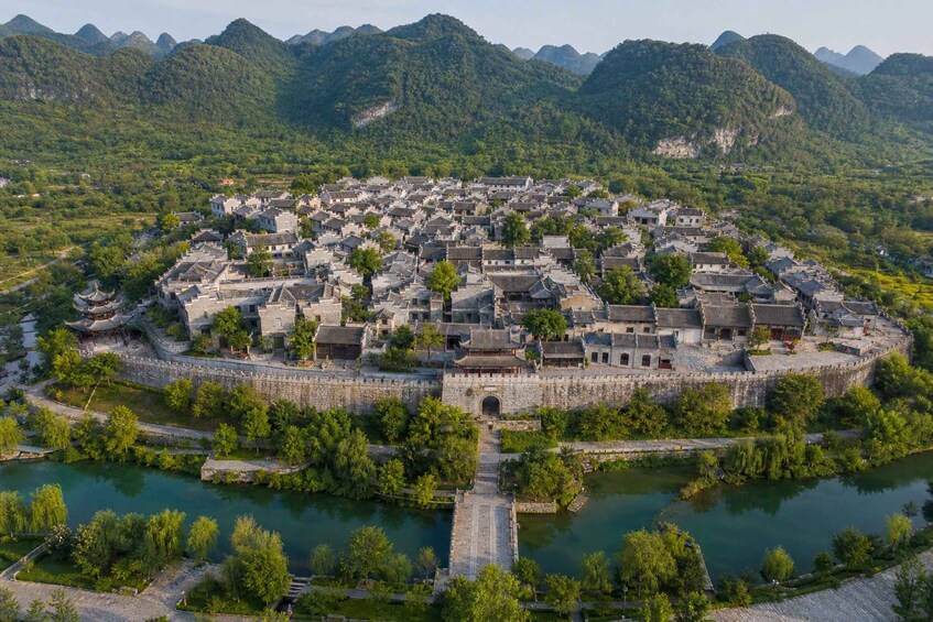 A traditional walled town with a river in the foreground, surrounded by lush green mountains. 5