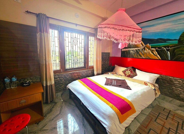 A bedroom with a bed, a red headboard, a painting, a window with bars, a wooden dresser, and a red chair. 2