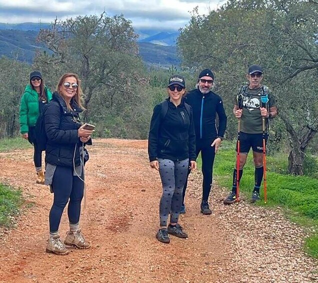 Un groupe de personnes fait de la randonnée sur un sentier de terre, entouré d’arbres et de collines. 2