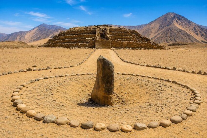 A desert landscape with a large stone structure, a circular arrangement of stones, and mountains in the background. 4