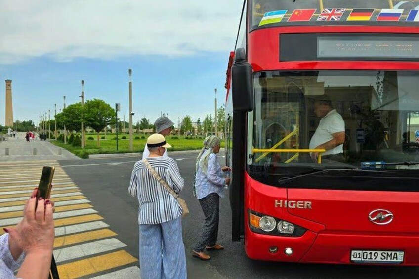 A red Higer bus at a bus stop with passengers waiting and a person taking a photo. 3