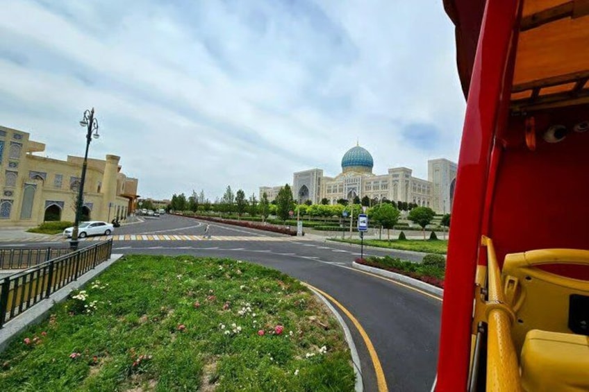 A road with a roundabout, a large building with a dome, and a red vehicle. 4