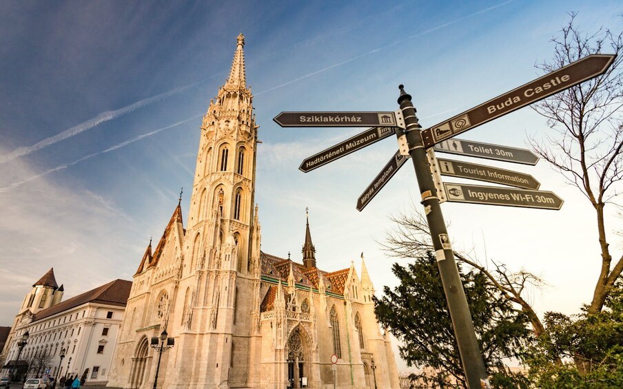 Una catedral histórica con una aguja puntiaguda, un indicador direccional con varios destinos, y un cielo despejado. 2
