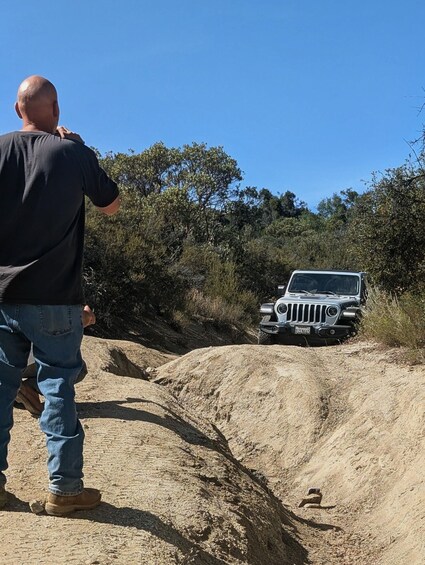 A person taking a photo of a vehicle on a dirt road with trees in the background. 5