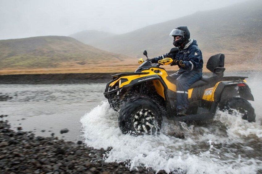A person riding a yellow ATV on a river surrounded by hills. 1