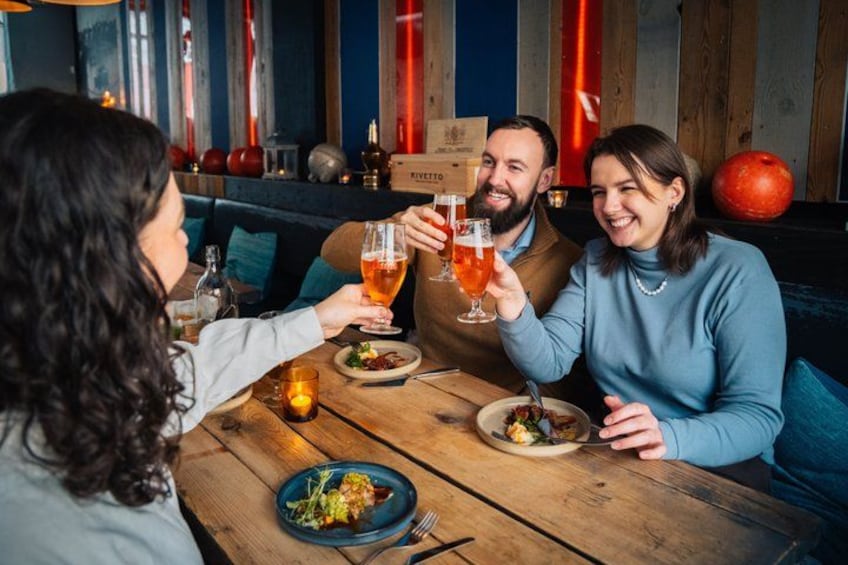 A group of people toasting with drinks at a wooden table in a restaurant with a rustic decor. 2