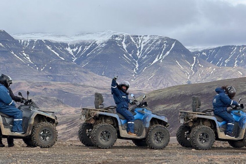 Three people on ATVs in a mountainous area with snow-capped peaks in the background. 4