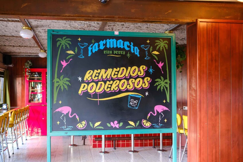 Una pizarra con texto y dibujos coloridos, incluyendo un flamenco y un vaso de cóctel, en un ambiente de cafetería. 2