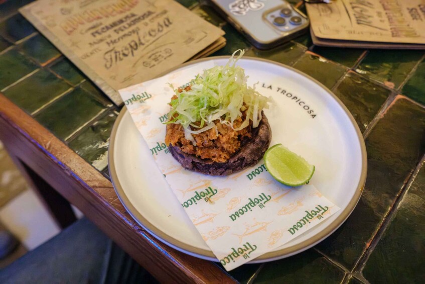 Un plato de comida con lechuga rallada encima, una cuña de lima y un papel con la marca 'La Tropica'. 4